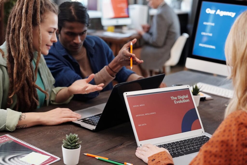 Team collaborating around laptops showing "The Digital Evolution" presentation in a modern marketing agency office.