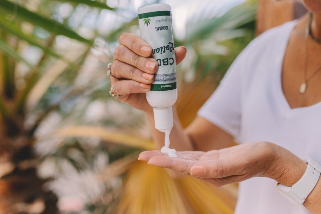 Woman dispensing CBD lotion from a 1000mg pump bottle into her palm outdoors near tropical plants.